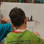 Drei Kinder stehen vor einer großen Leinwand und malen auf diese.