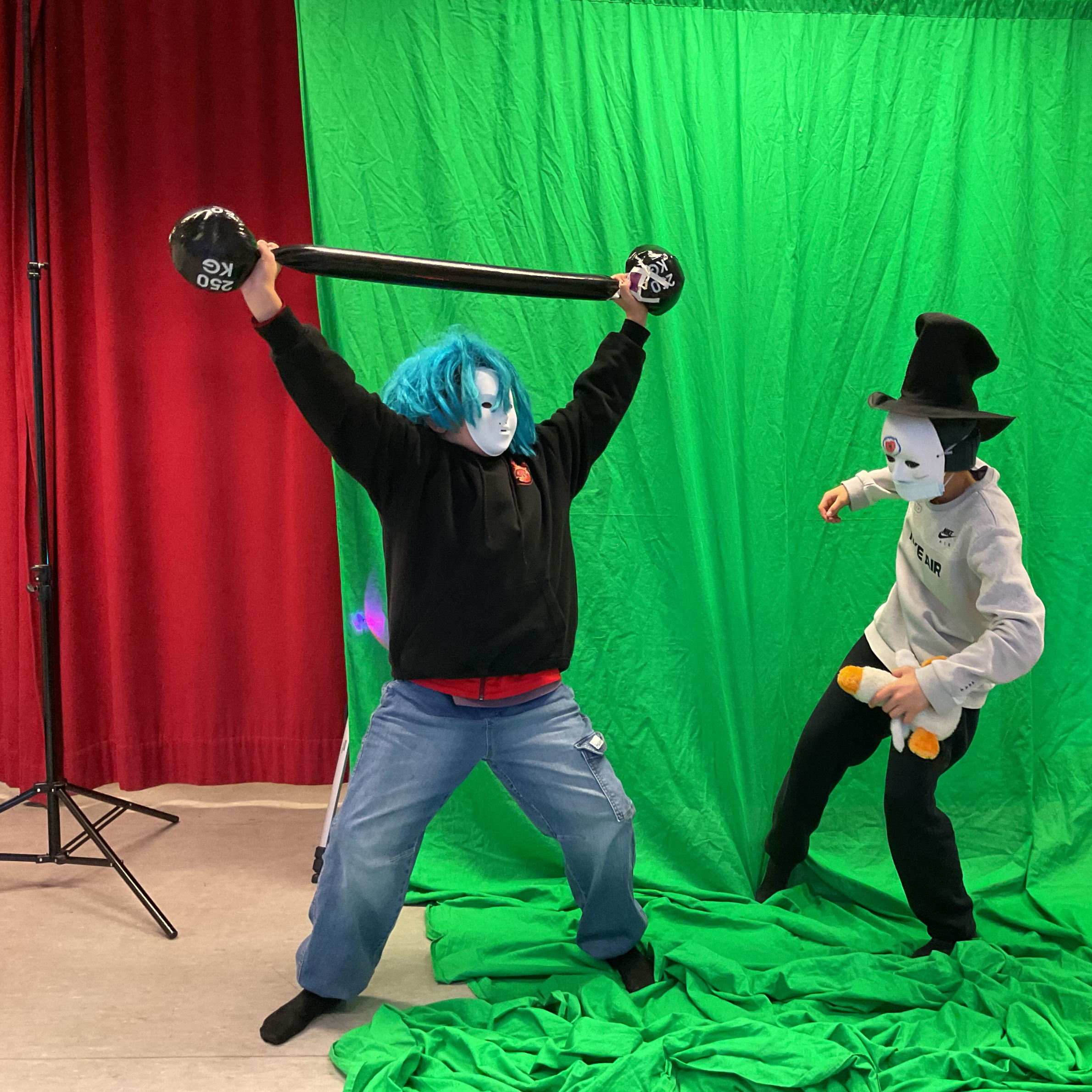 Zwei Kinder mit weißen Masken schauspielern vor einer grünen Wand.