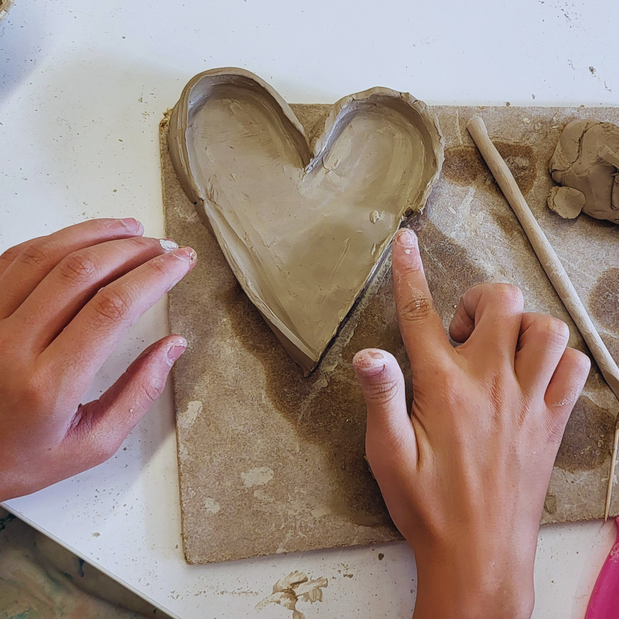 Hände formen eine Tonschale in Herzform.